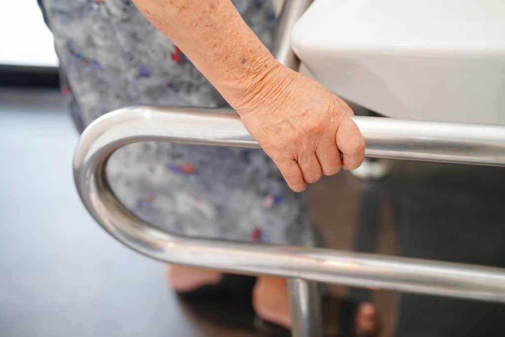 An elderly person using a handrail in the bathroom. Accesibility is an important feature for tubs for seniors.